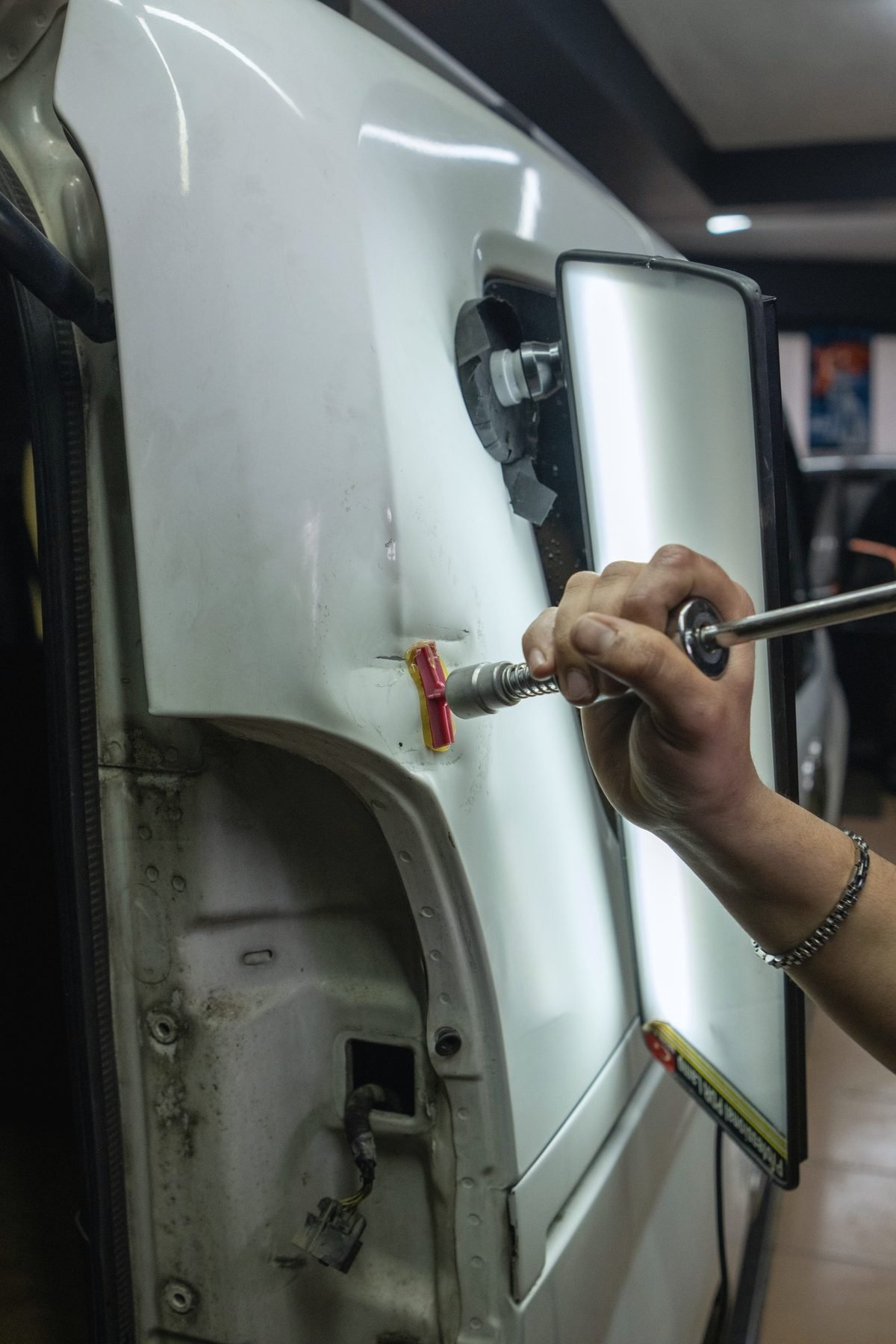 A hand working a dent out of a light-coloured door panel with a puller