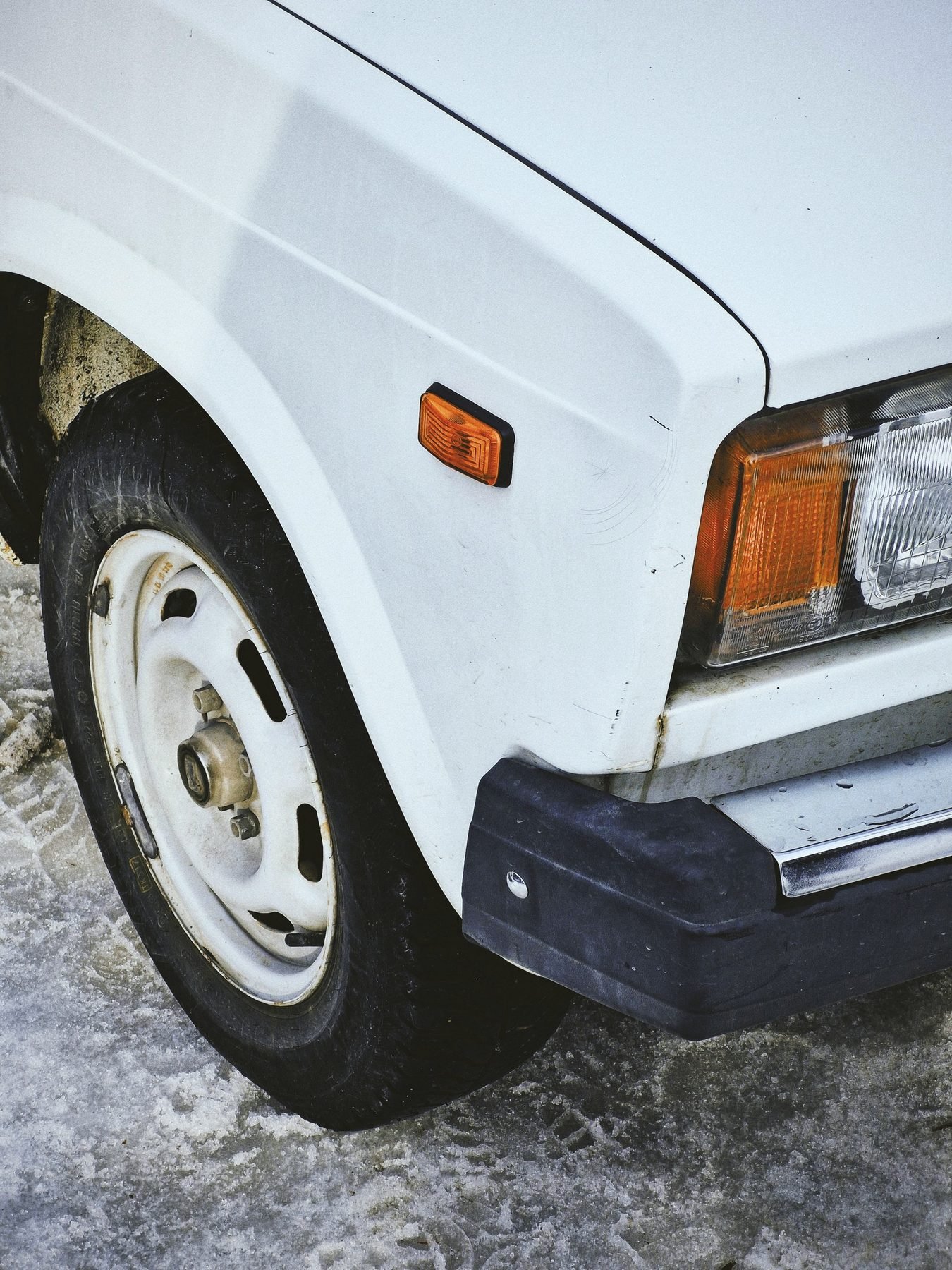The front fender and wheel of a white car parked on salted, slushy snow