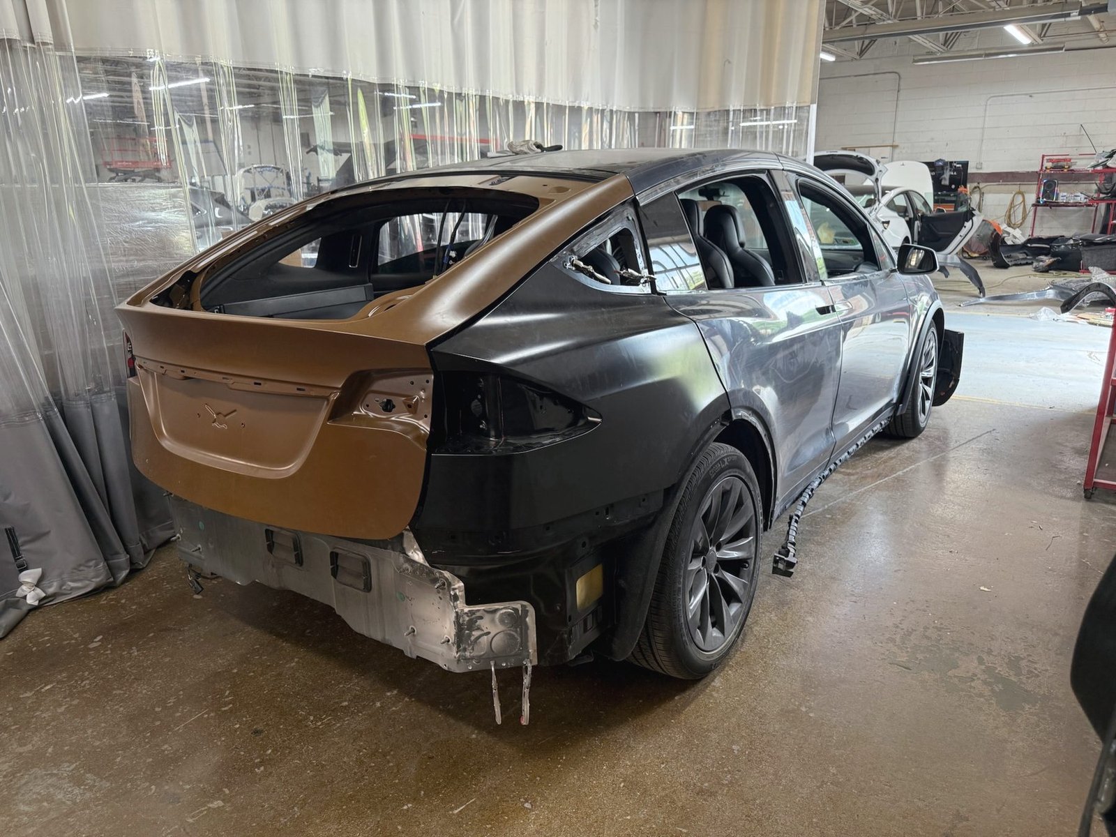 A car in a repair bay with its rear end stripped to bare panels and new metal fitted