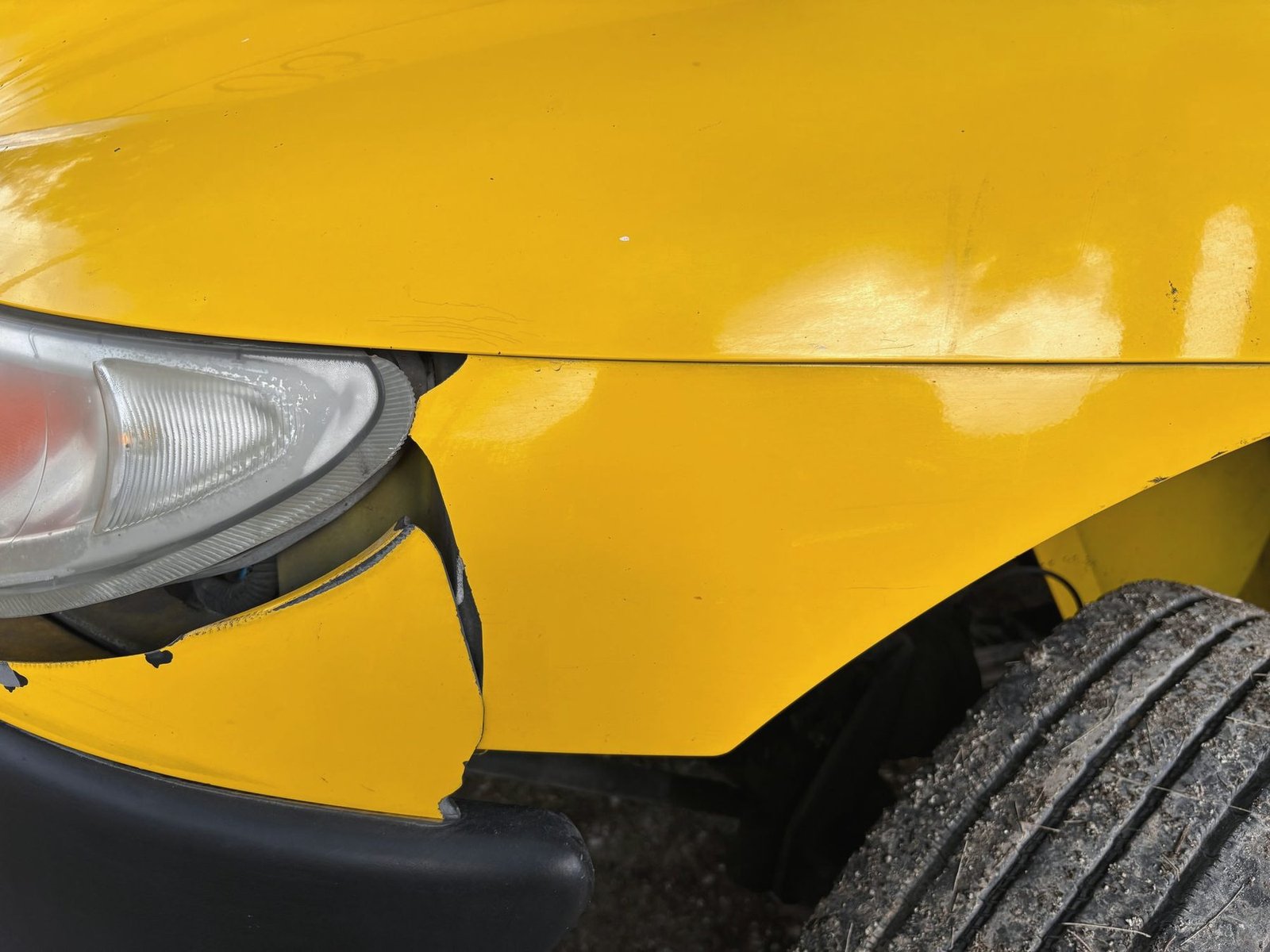 A yellow bumper cover split at the headlight, pushed back toward the wheel