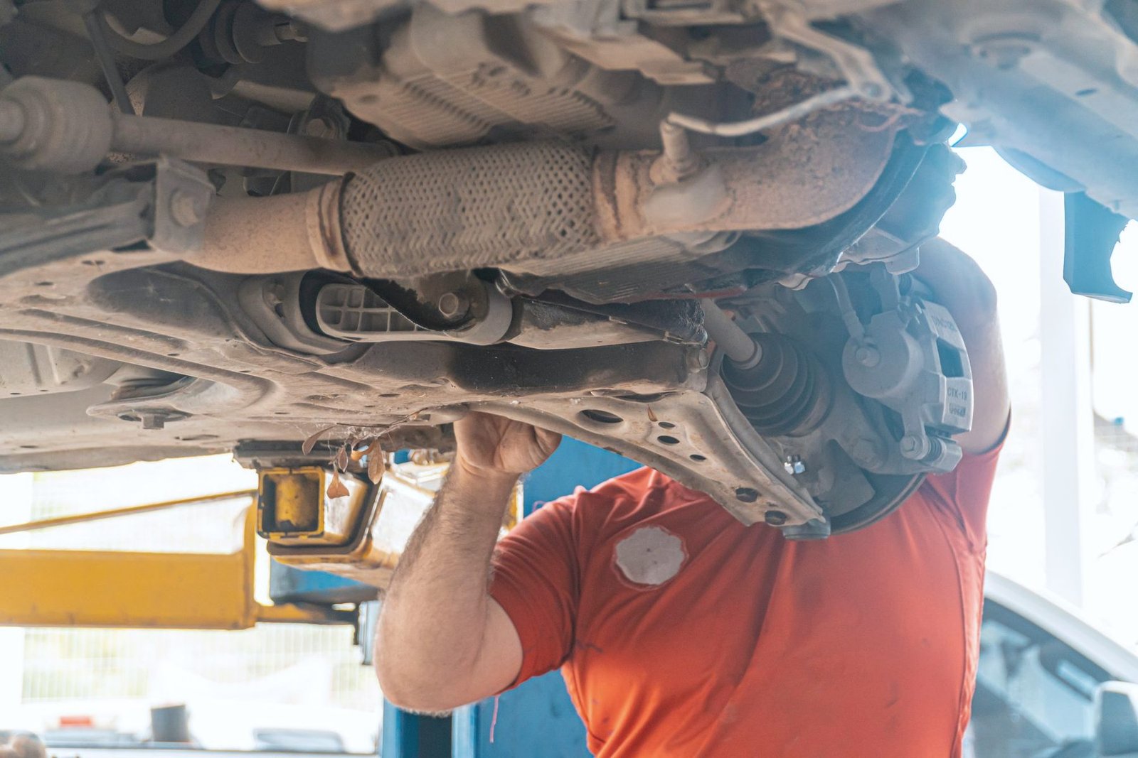 A worker under a lifted car with the exhaust and suspension overhead